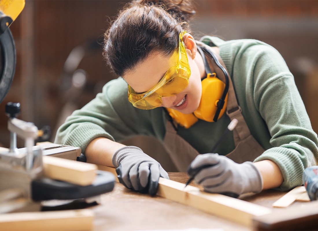 Insurance by Industry - Female Carpenter in Her Workshop Marking Up Wood While Smiling